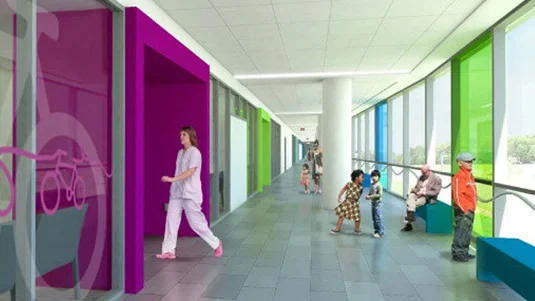 A woman in a white shirt walks down a hospital hallway with a child.