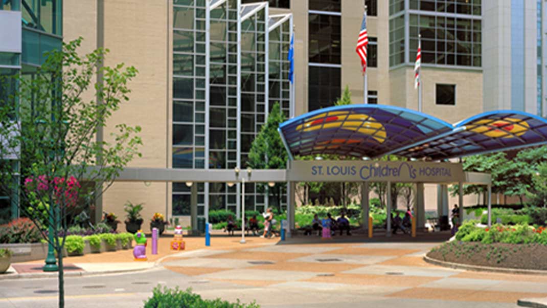 Entrance of St. Louis Children's Hospital with a colorful glass canopy and flags in front of a multi-story building.